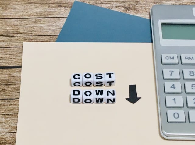 電卓の横に「COST DOWN」の文字と下向きの矢印を並べた、コスト削減のイメージ写真