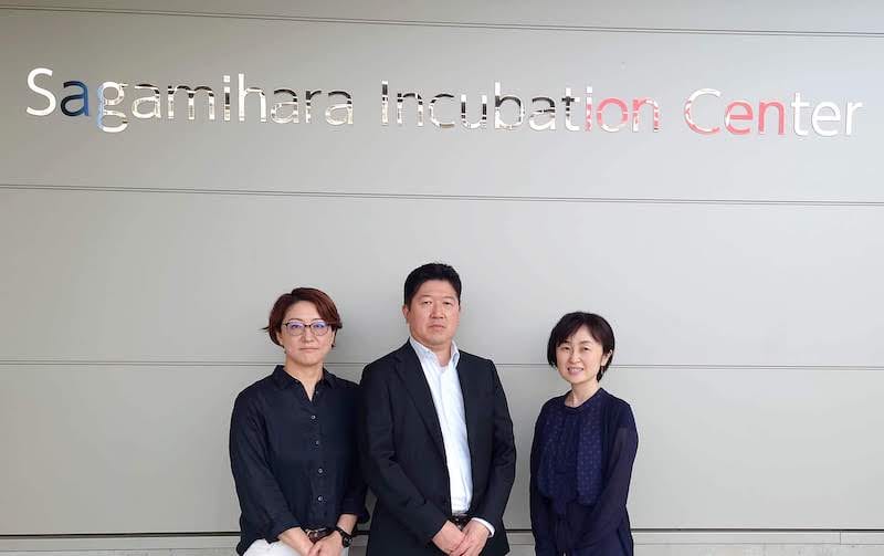 Sagamihara Incubation Center の看板の前に立つ、エム・アイ・エス テクノロジー株式会社のご担当者 3 名の写真